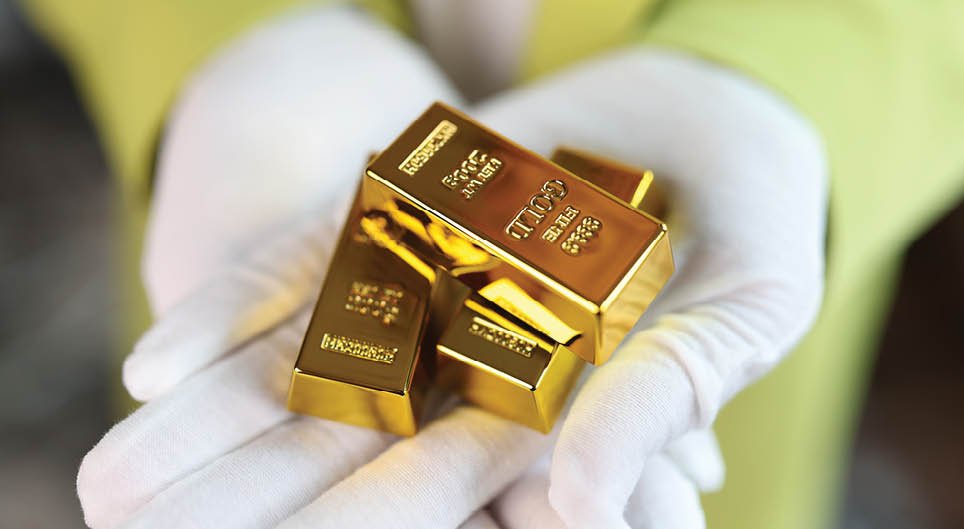 Close-up of man holding gold bars in his hands. Several gold bars in hands of person in white gloves.